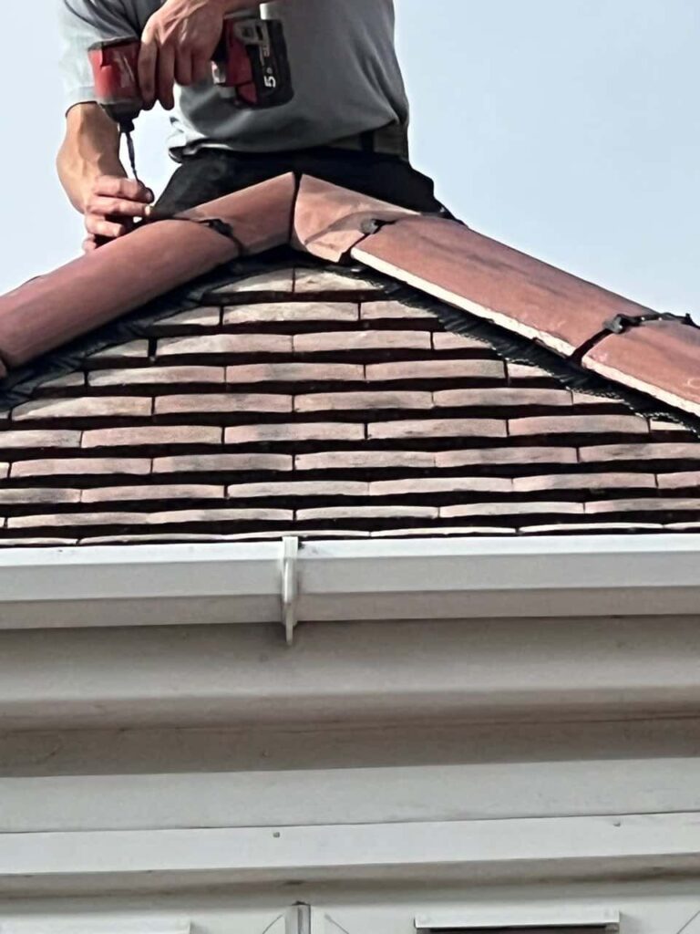 This is a photo of one of the operatives of Cambourne Roofing Repairs installing new ridge tiles